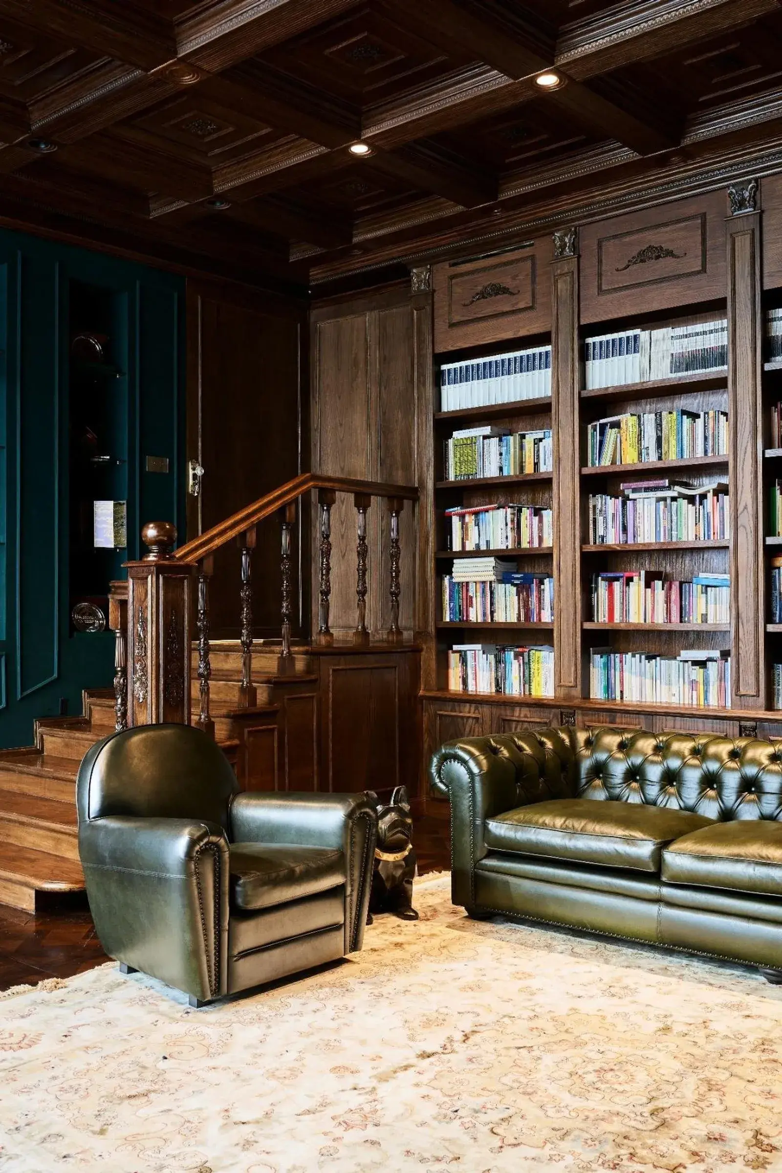 Bibliothèque en bois massif, plafond à caissons et fauteuils chesterfield en cuir vert