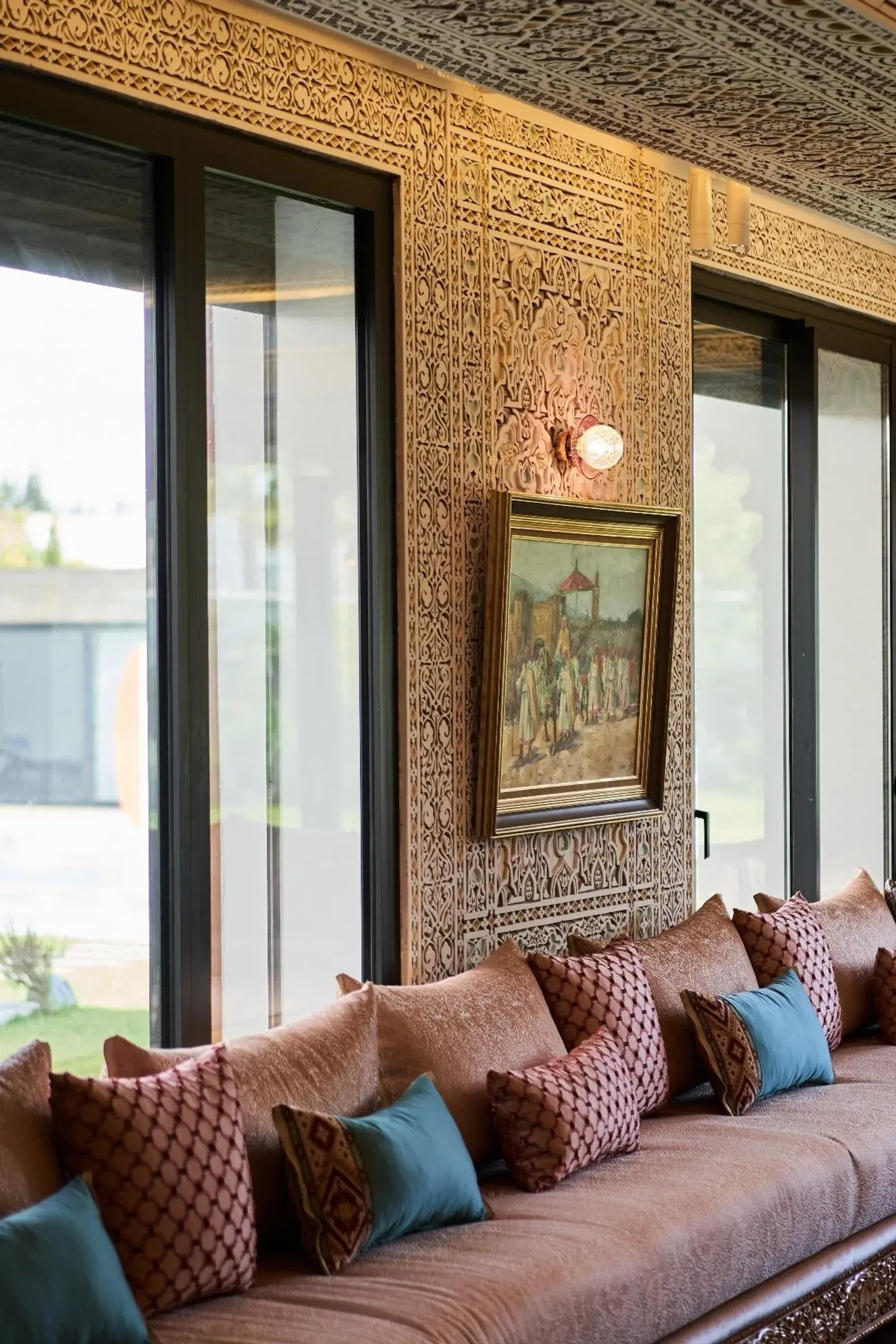 Banquettes en velours terracotta et bleu canard sous les murs sculptés du salon marocain